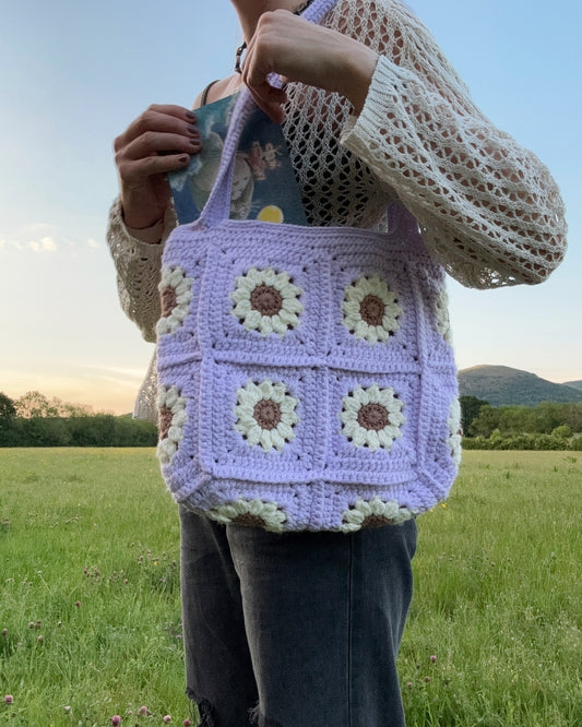 Daisy tote bag crochet pattern, floral market bag, PDF download, beginner-friendly, Easy to Crochet. In lots of different colors. Girl is standing wearing Daisy Tote Bag.