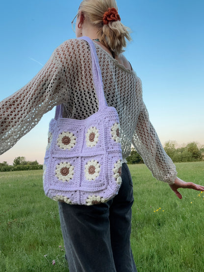 Daisy tote bag crochet pattern, floral market bag, PDF download, beginner-friendly, Easy to Crochet. In lots of different colors. Girl is standing wearing Daisy Tote Bag.