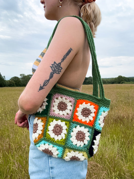 Daisy tote bag crochet pattern, floral market bag, PDF download, beginner-friendly, Easy to Crochet. In lots of different colors. Girl is standing wearing Daisy Tote Bag.