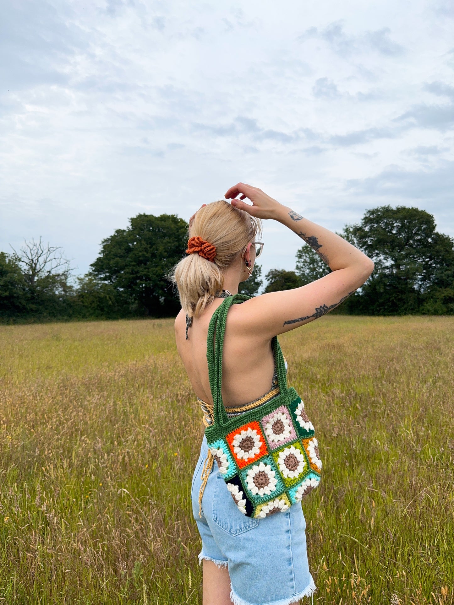 Daisy tote bag crochet pattern, floral market bag, PDF download, beginner-friendly, Easy to Crochet. In lots of different colors. Girl is standing wearing Daisy Tote Bag.