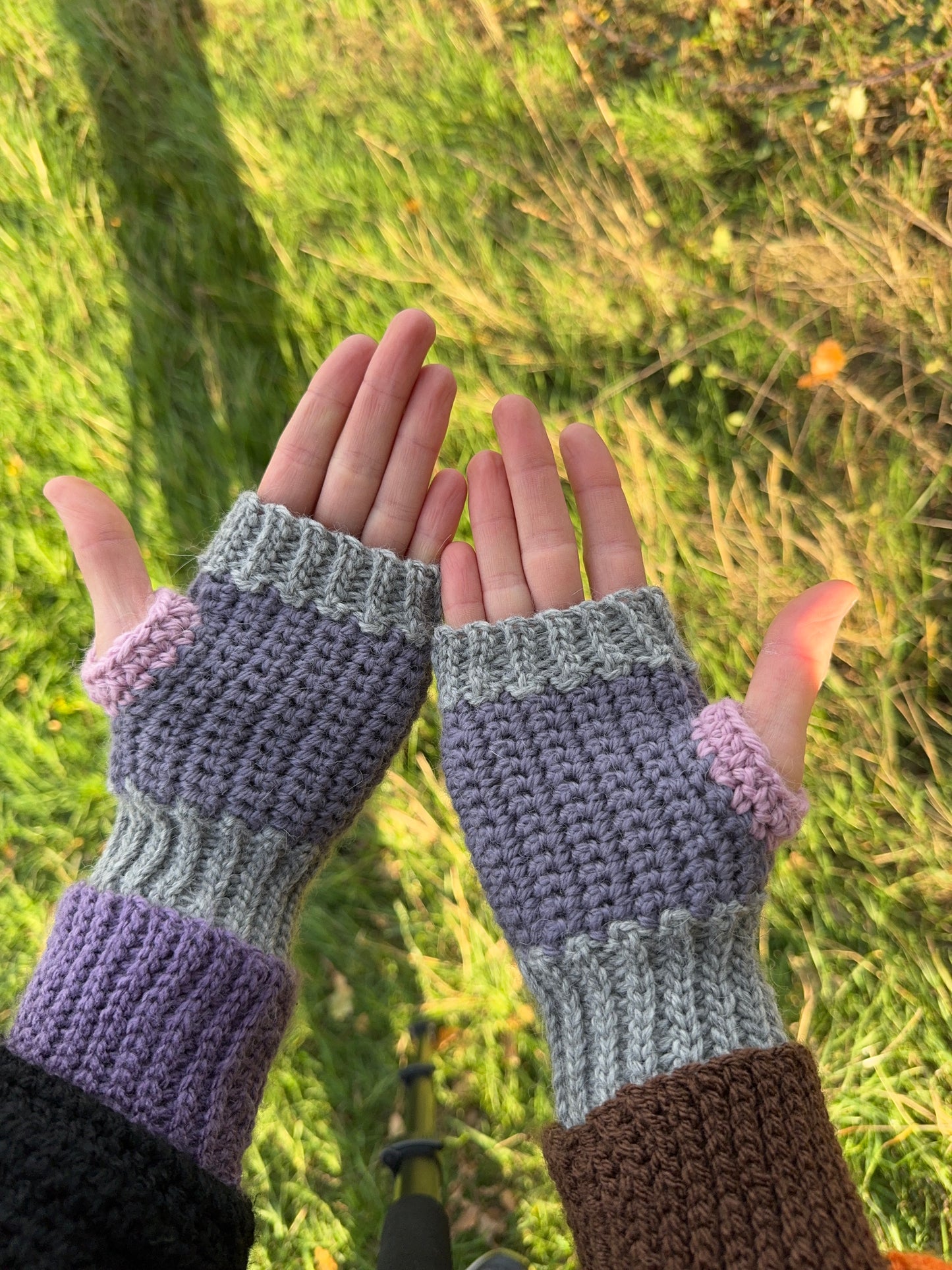 Fingerless gloves crochet pattern – textured handmade wrist warmers in pink and purple color shades, showing palm side of the glove. Easy beginner crochet project with a step-by-step picture tutorials.