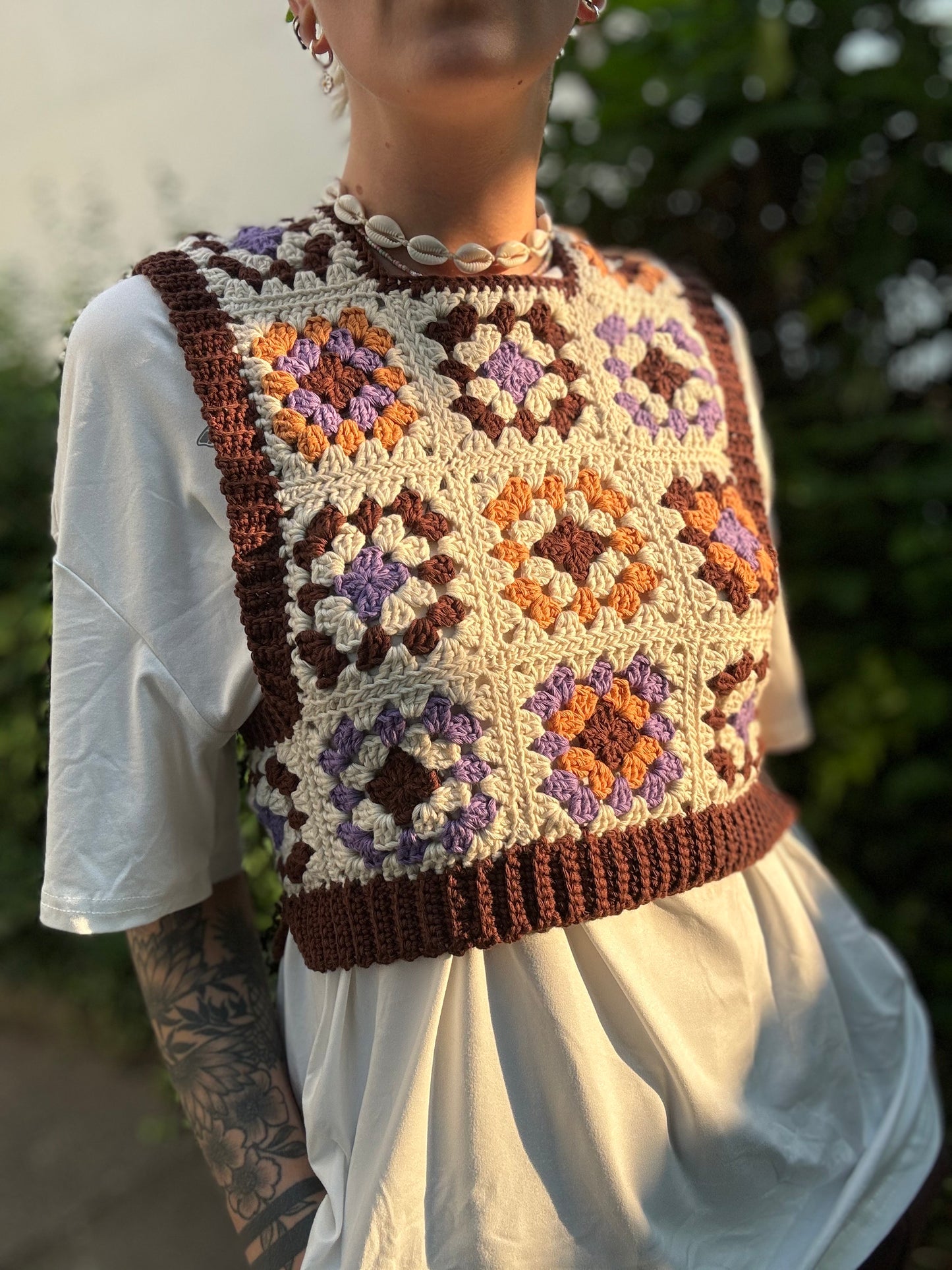 Crochet Pattern Picture of granny square patchwork top which crochet business owner wears in on top of white shirt outside.