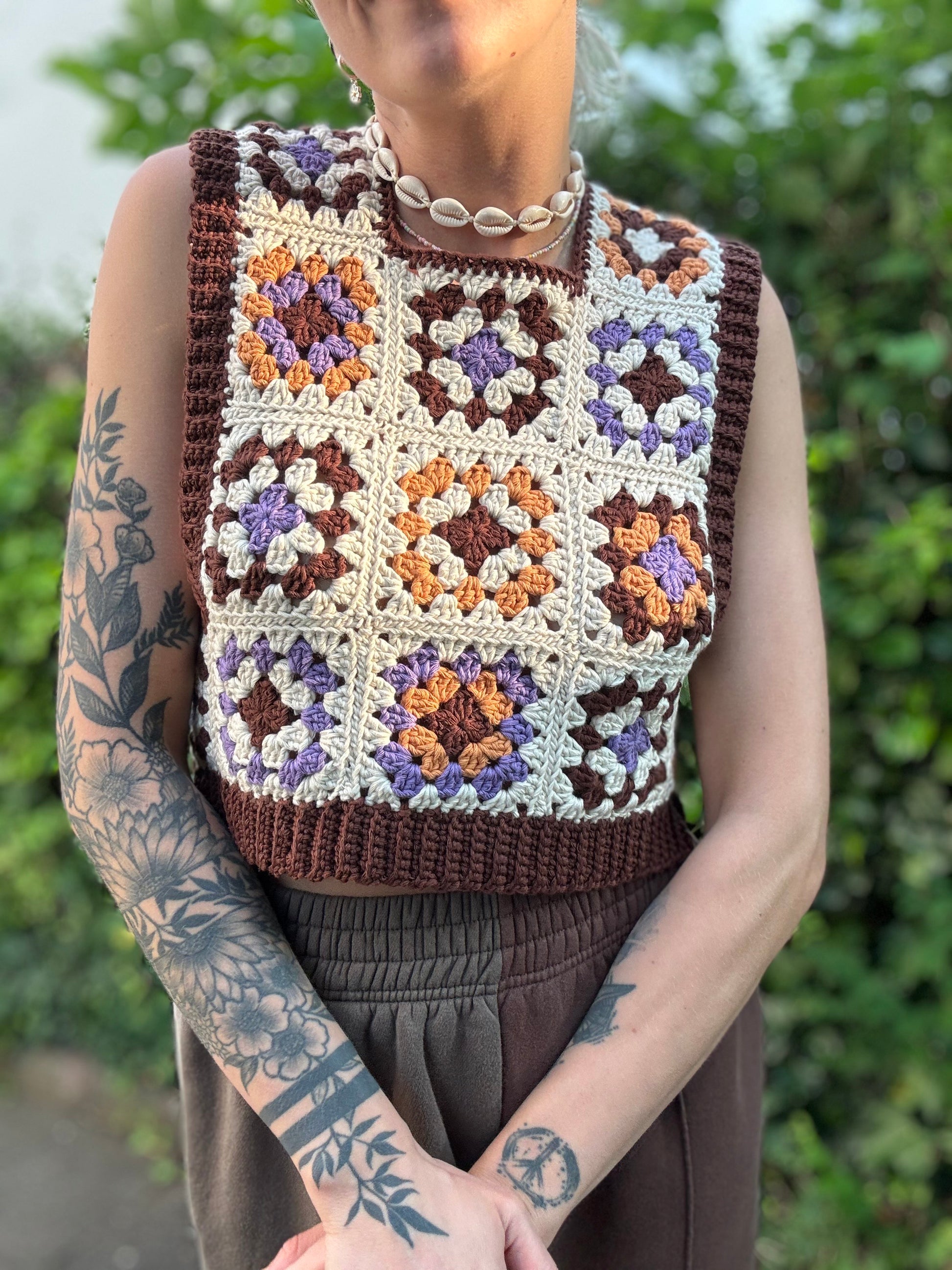 Crochet Pattern Picture of granny square patchwork top which crochet business owner wears in on top of white shirt outside.