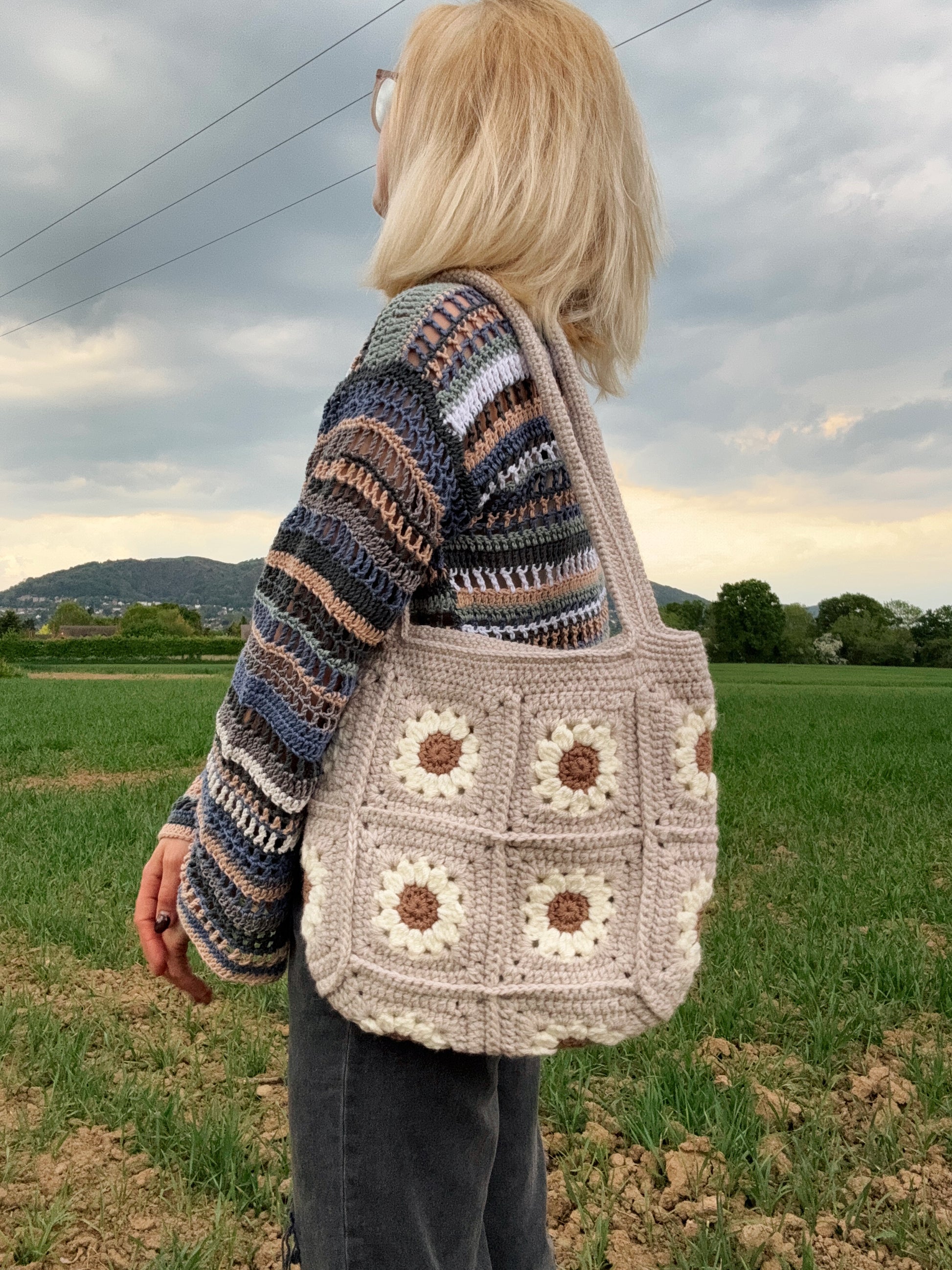 Daisy tote bag crochet pattern, floral market bag, PDF download, beginner-friendly, Easy to Crochet. In lots of different colors. Girl is standing wearing Daisy Tote Bag.